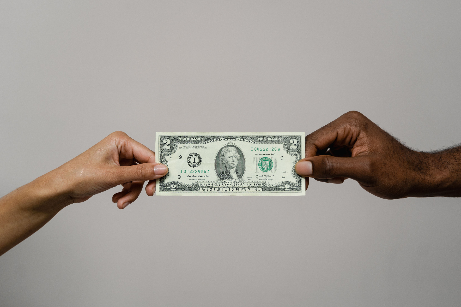 Two hands passing a two-dollar bill a simple exchange.